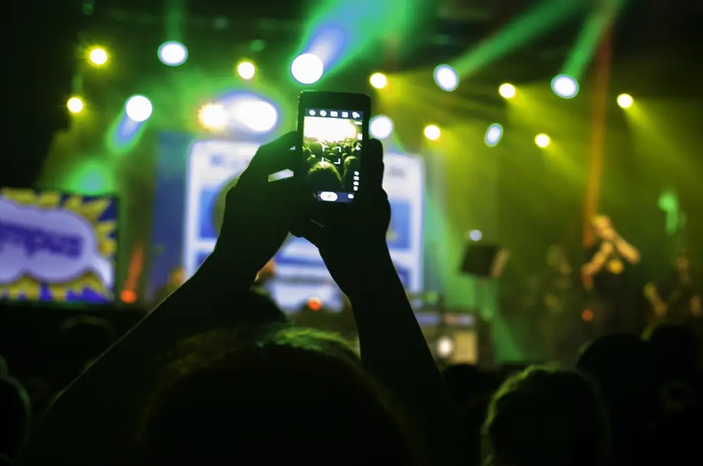 Persona grabando con el celular en alto durante un concierto con luces de escenario, referencia al contenido de shows en vivo en Instagram Chile