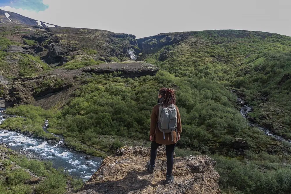 Mochilera frente a un valle verde con un río de montaña, referencia al contenido de viajes y naturaleza en Instagram Chile