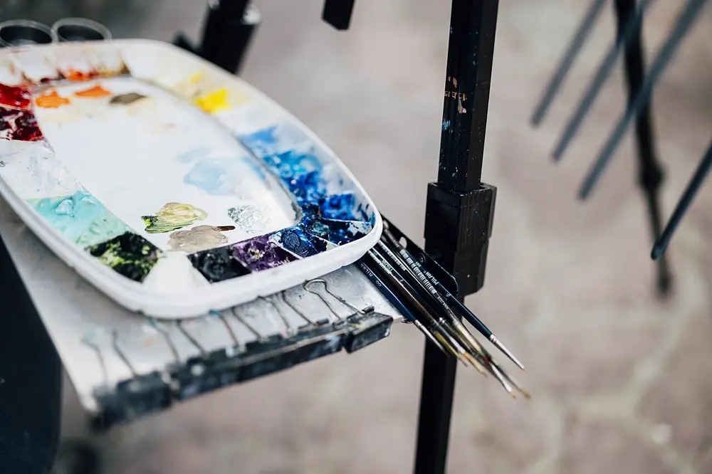Paleta de pintura con colores mezclados y pinceles junto a un atril, referencia al contenido de arte y pintura en Instagram Chile