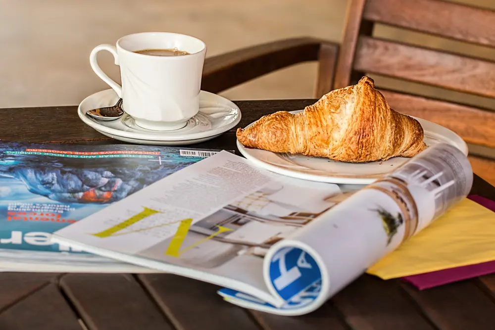 Taza de café con croissant y revistas en una mesa de terraza, referencia al contenido lifestyle en Instagram Chile